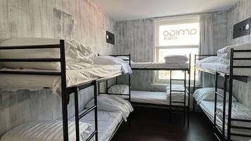 A dormitory room with bunk beds, a window with curtains, and a visible ceiling light fixture.