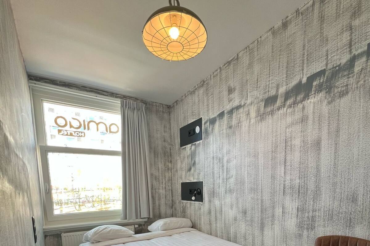 Quarto com cama, cadeira, janela com cortinas, luminária na parede e radiador.