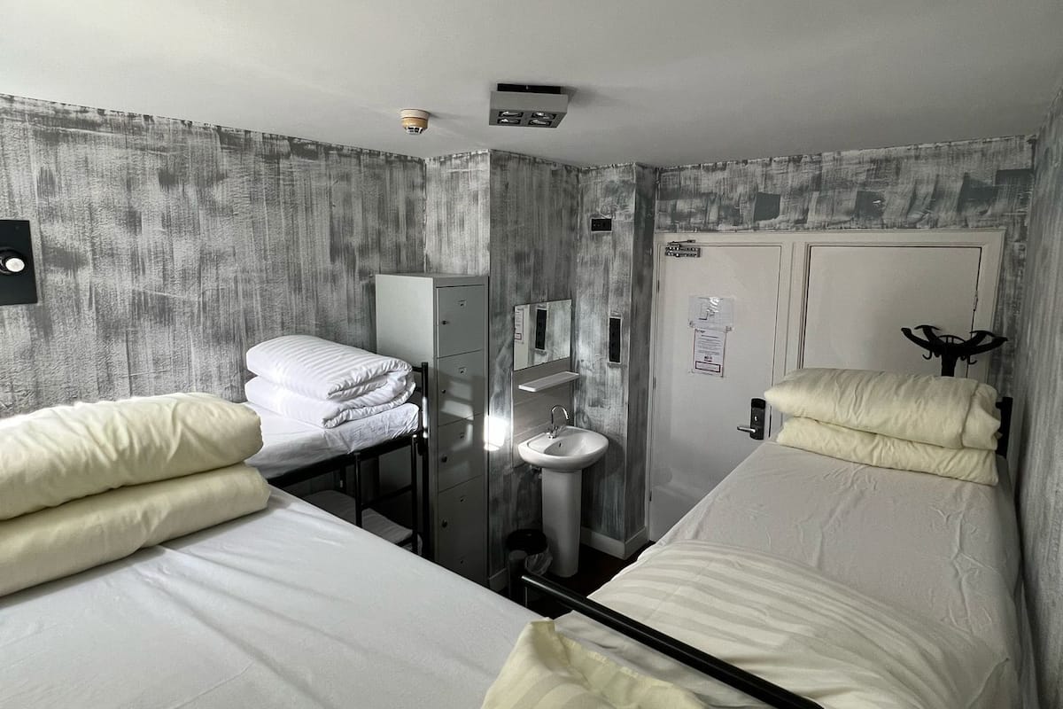 A hotel room with two beds, a sink, a mirror, and a wardrobe.