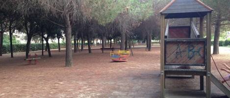A park with a playground, including a swing set and a slide, surrounded by trees.