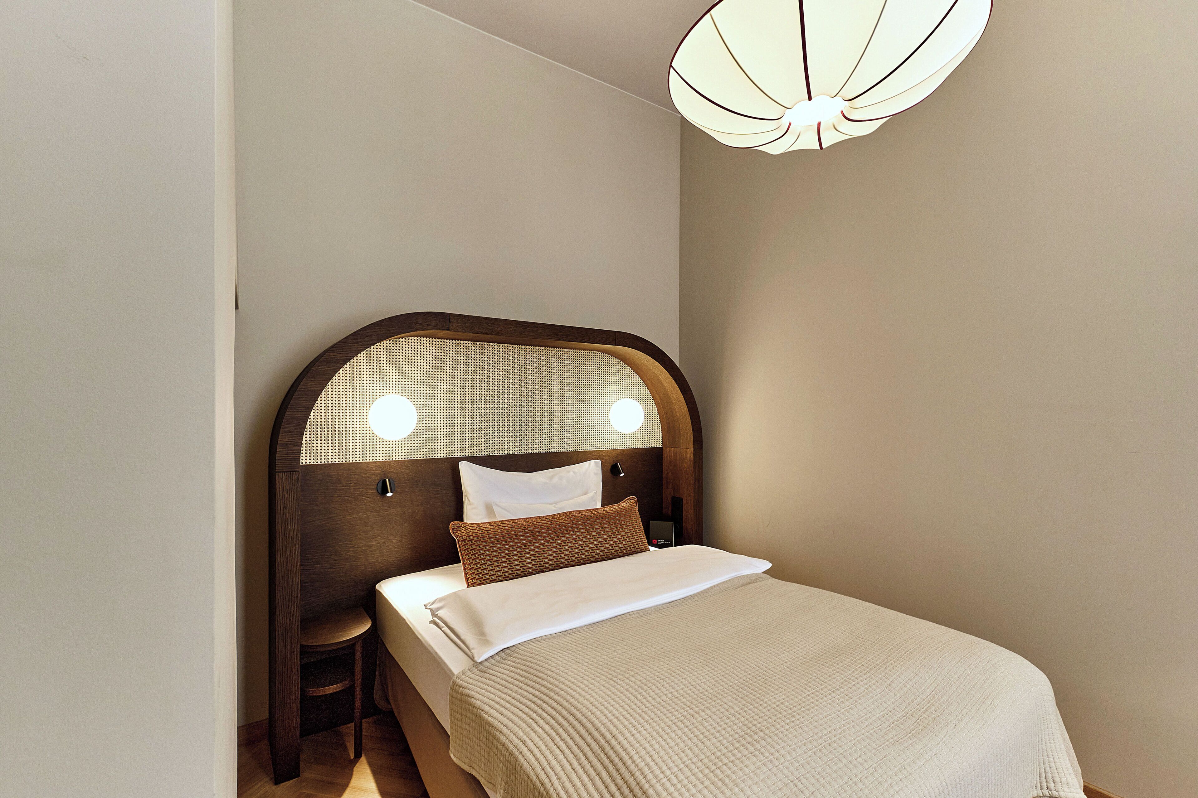 A neatly made bed with a wooden headboard, a bedside table, and a wall-mounted light fixture.