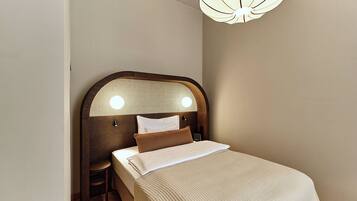A neatly made bed with a wooden headboard, a bedside table, and a wall-mounted light fixture.