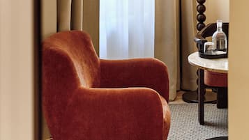 Una habitación de esquina con un sillón rojo, una lámpara y una mesita con una botella y una taza.