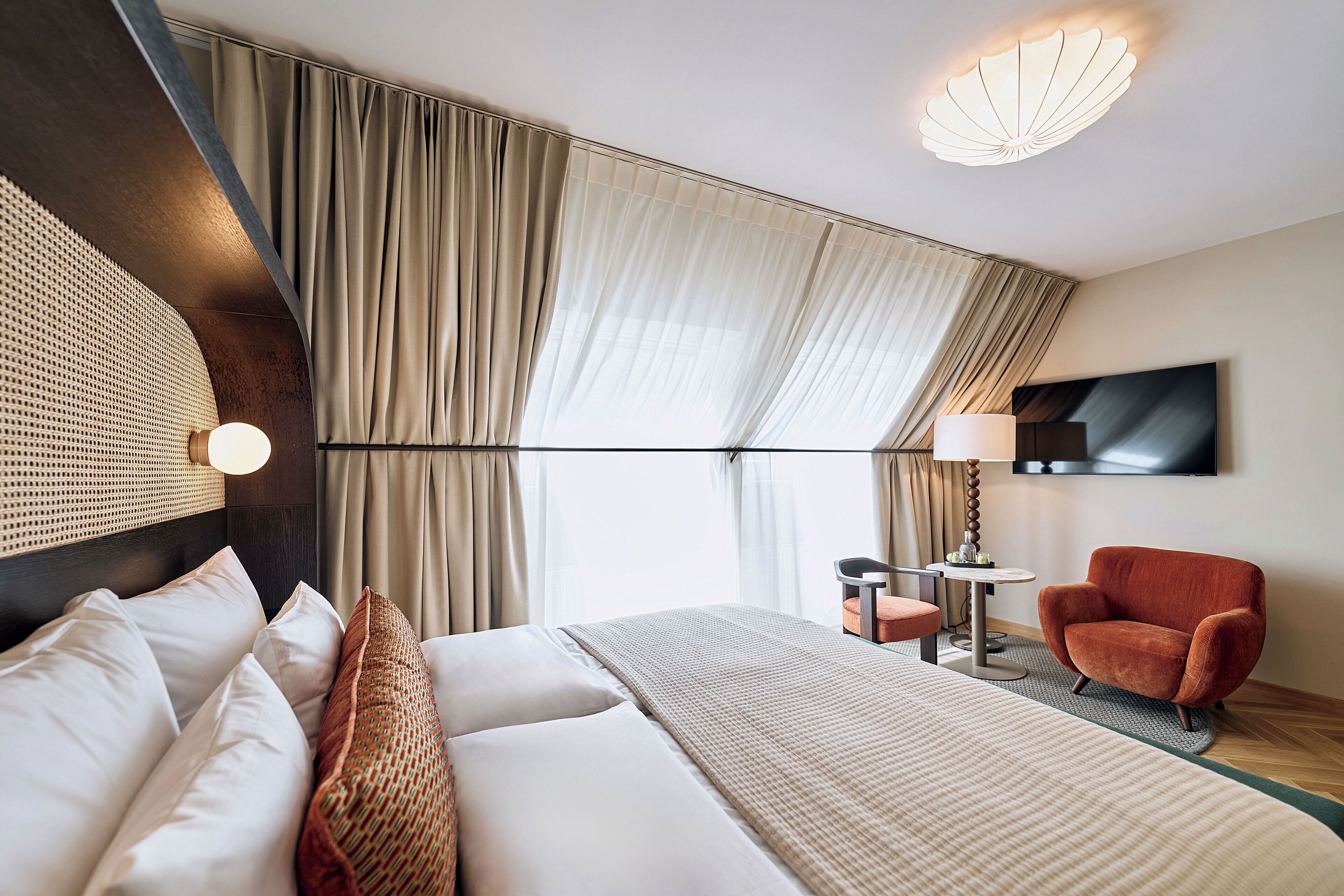 Une chambre d’hôtel moderne dotée d’un grand lit, d’un téléviseur fixé au mur et d’un coin salon avec une chaise et une table.