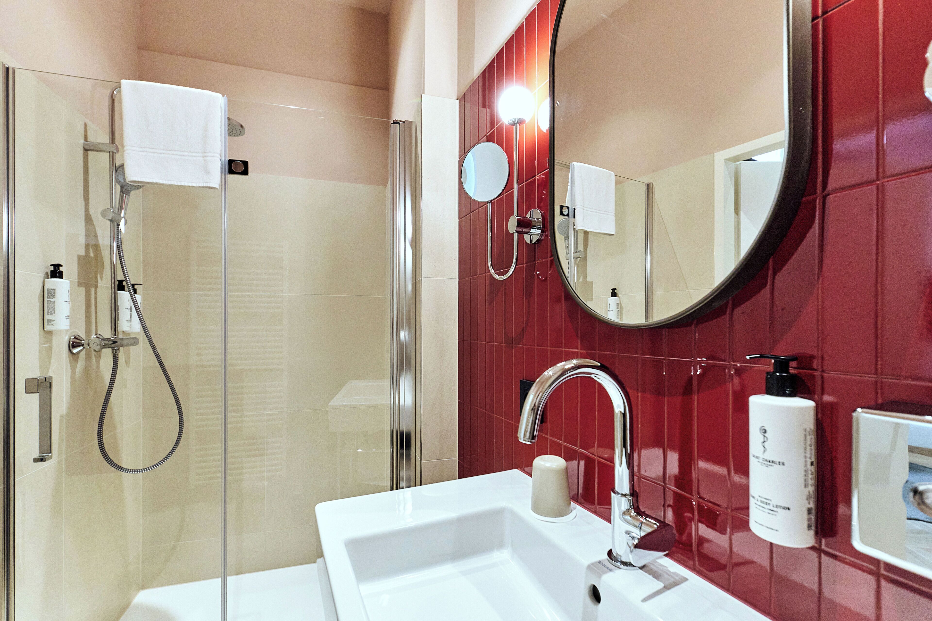 Et badeværelse med en glasvæg omkring brusebadet, en hvid vask, et spejl og røde fliserede vægge.