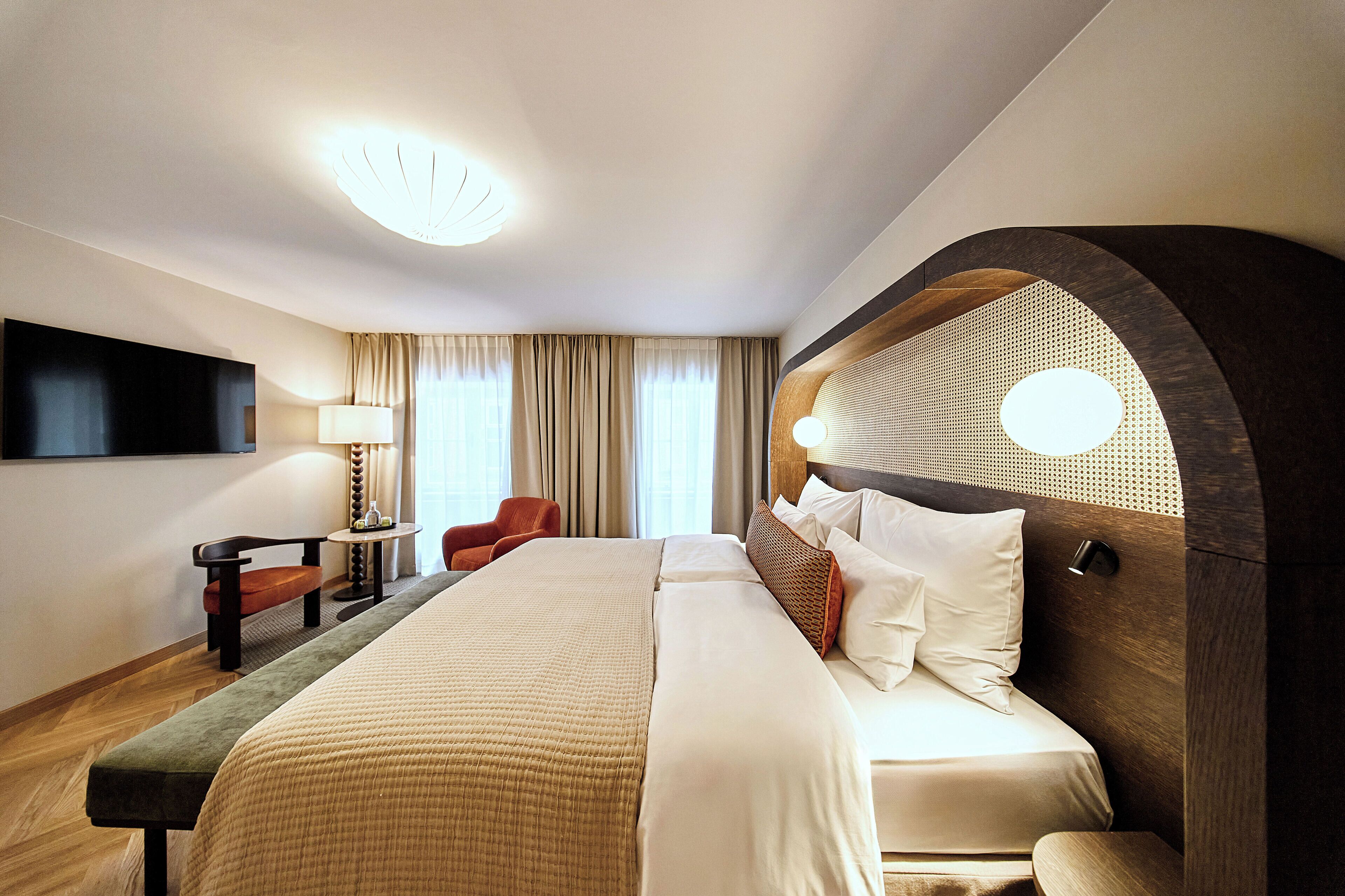 A hotel room with a large bed, a desk, a chair, and a TV on the wall.