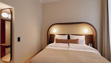 A neatly made bed with a headboard, a mirror, and a bedside table with a lamp.