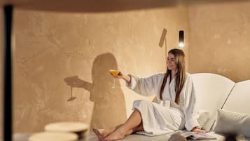 A person sitting on a bed in a room with a textured wall, holding a drink.