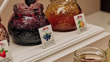 A hand holding a chopstick with a piece of food, a jar of blueberry jam, and a jar of apricot jam on a shelf.