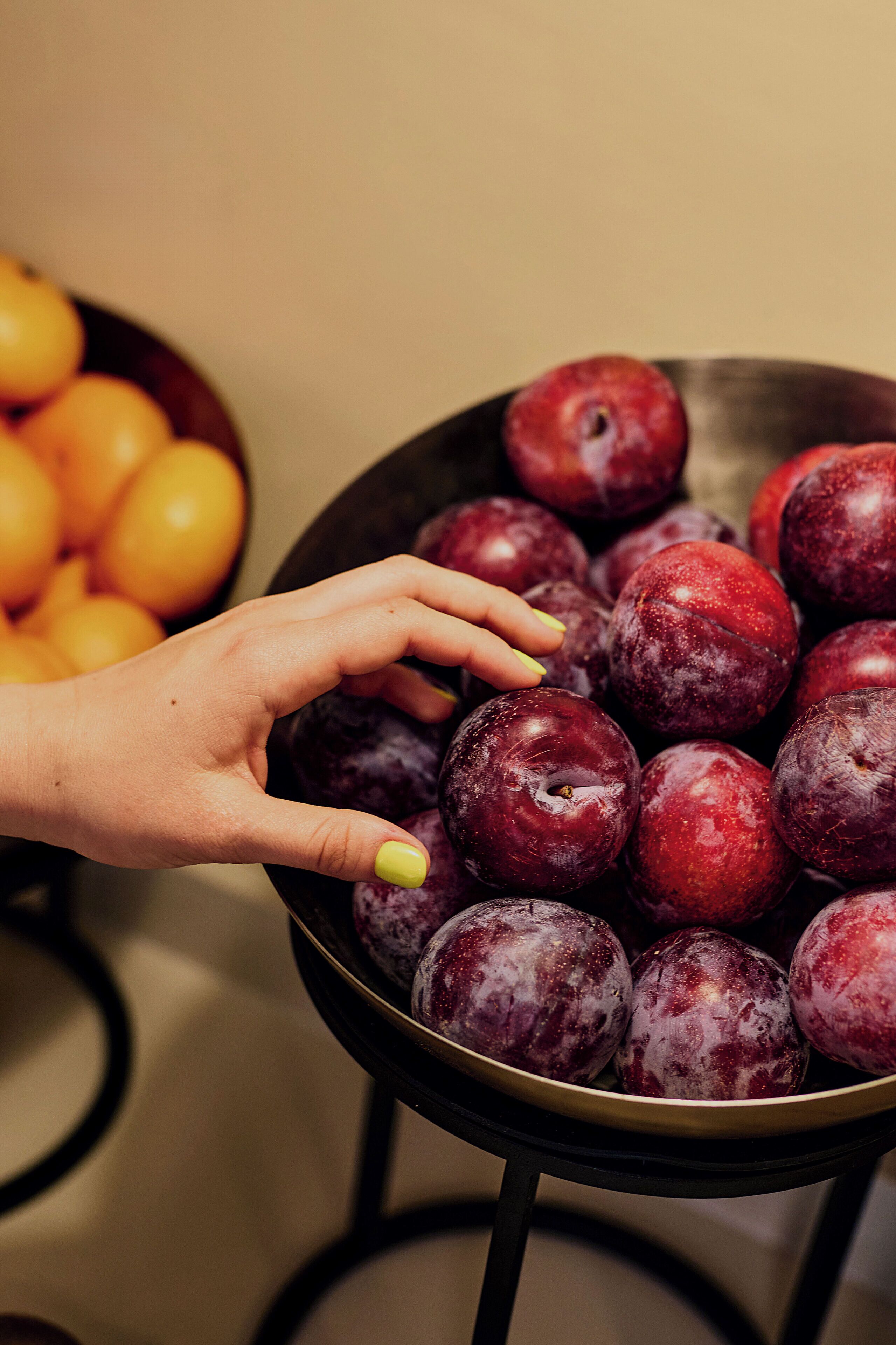 A hand reaching for plums in a bowl.