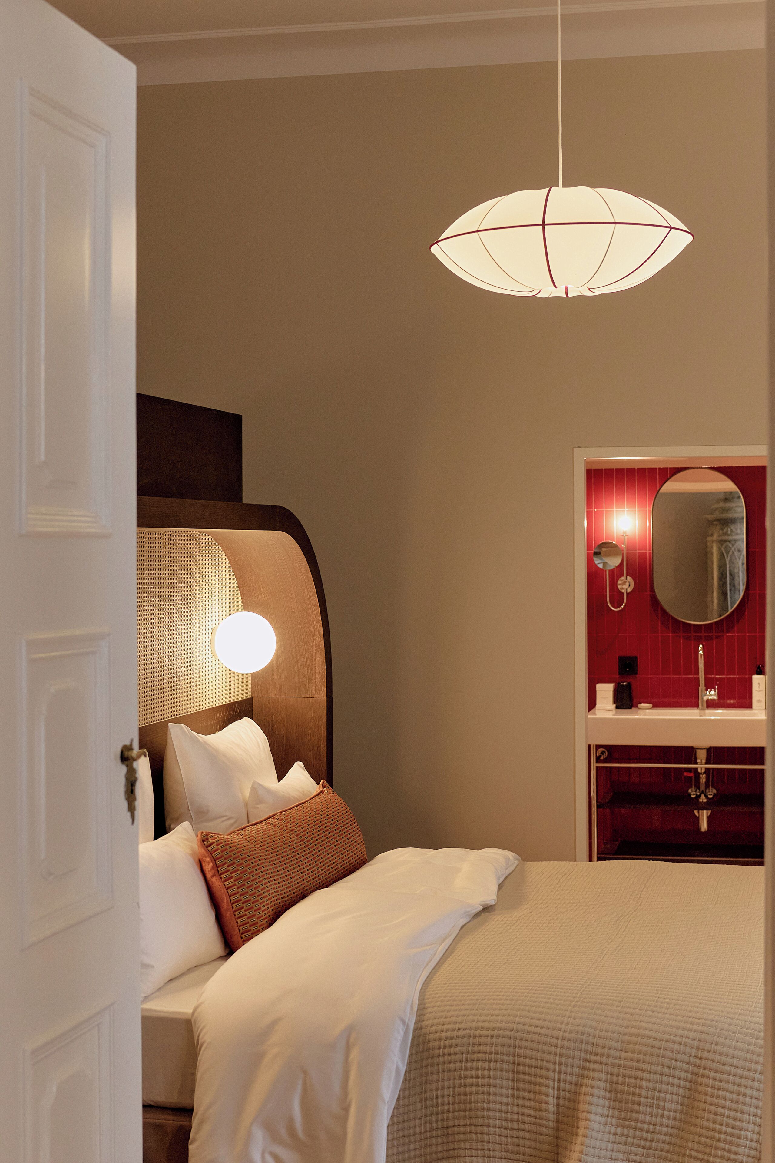 A hotel room with a bed, a bedside lamp, a mirror, and a hanging light fixture.