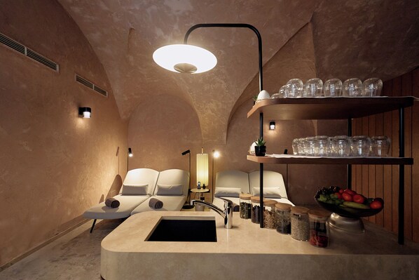 Une salle de spa équipée d’un lavabo, d’étagères avec de la verrerie, d’un panier de fruits et d’une table de massage.