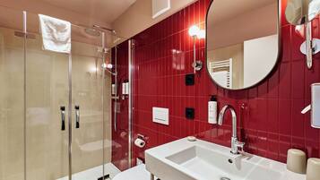 A modern bathroom with a glass shower enclosure, a white sink, and a red tiled wall.