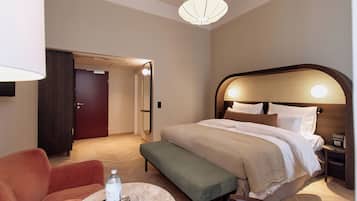 A hotel room with a bed, bedside table, lamp, and a seating area with a chair and bench.
