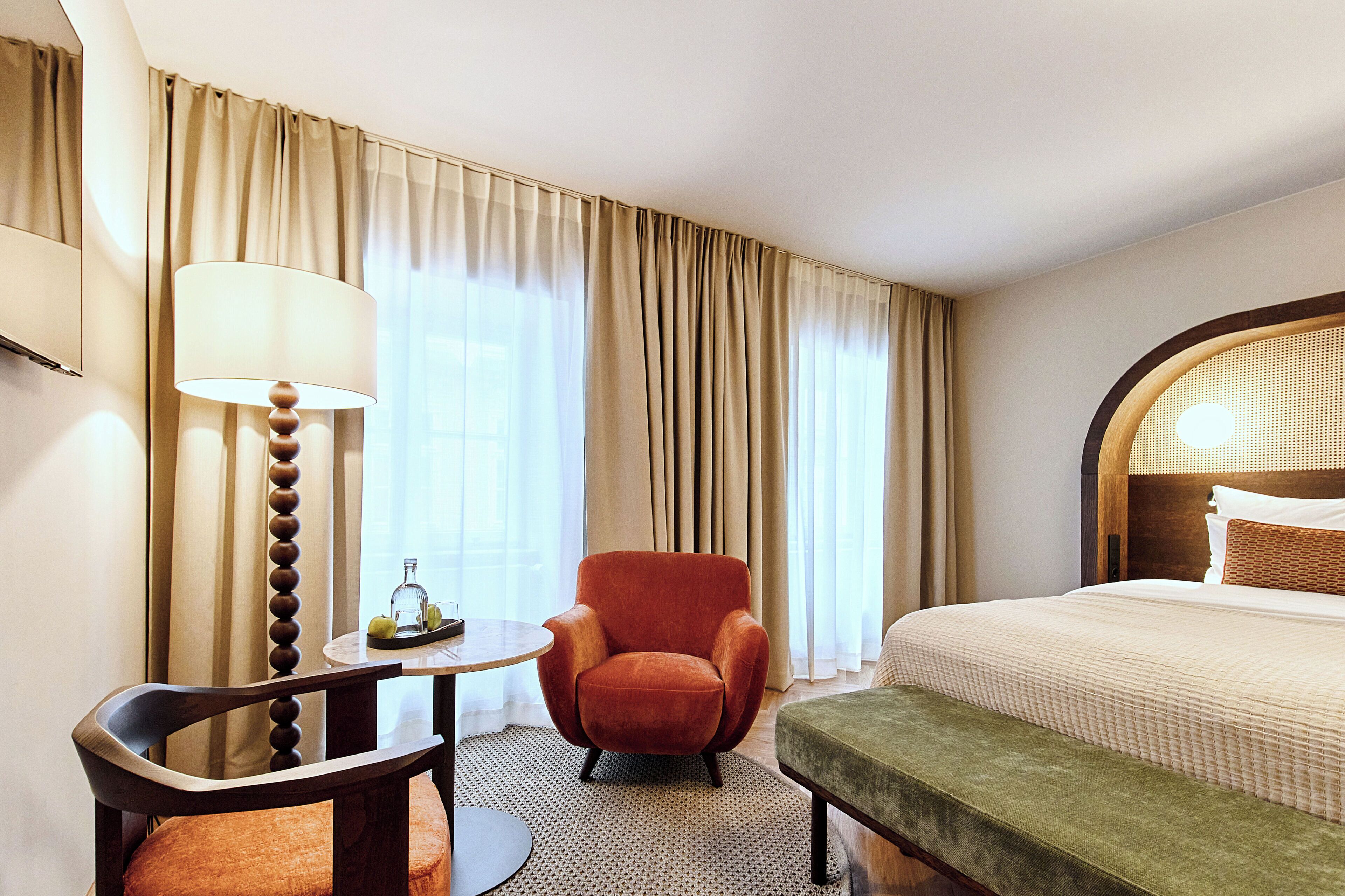 A hotel room with a bed, a chair, a table, and a lamp.