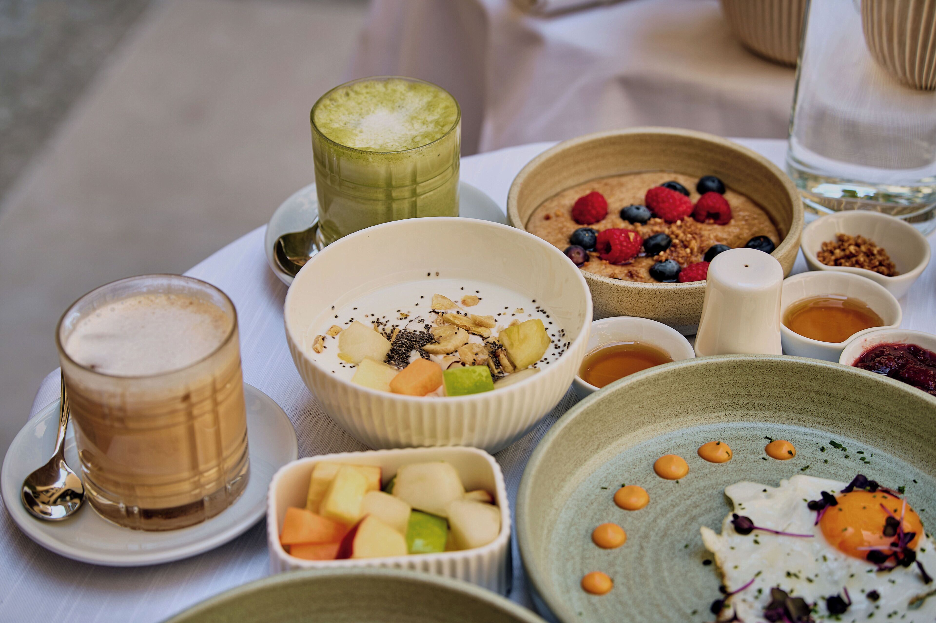 A variety of breakfast items including a glass of coffee, bowls of cereal with fruits, and a plate with an egg.