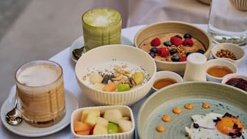 A variety of breakfast items including a glass of coffee, bowls of cereal with fruits, and a plate with an egg.