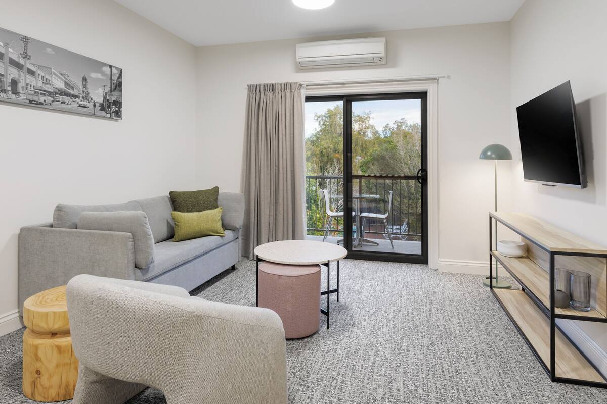 A modern living room with a grey sofa, round table, and a flat-screen TV.