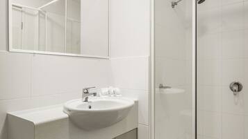 A modern bathroom with a white sink, mirror, and glass-enclosed shower.