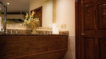 A wooden vanity with a mirror, a vase of flowers, and a sink with faucets.
