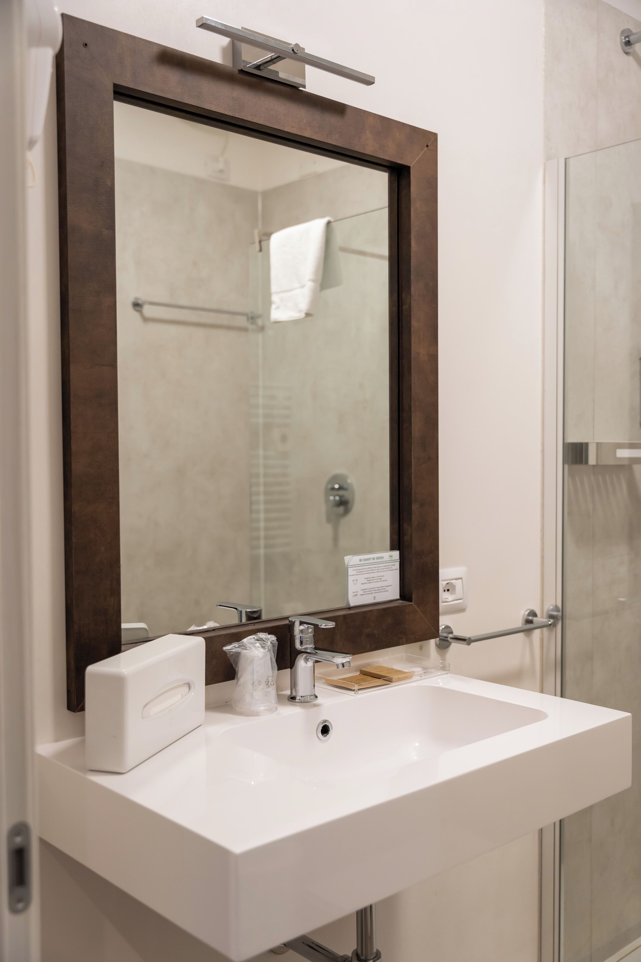 A bathroom with a white sink, a mirror with a wooden frame, a towel rack, and a glass shower enclosure.