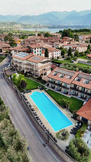 A hotel with a swimming pool, multiple balconies, and a view of the surrounding town and mountains.