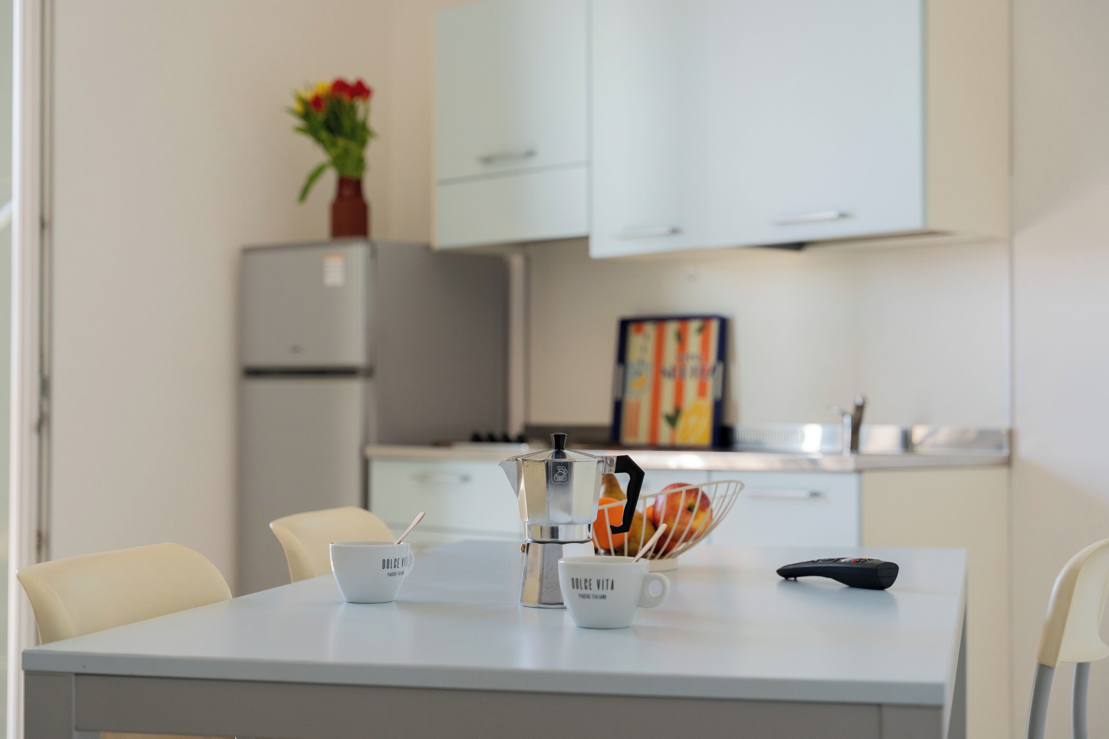 A modern kitchen with white cabinets, a coffee maker, and a fruit bowl on the counter.