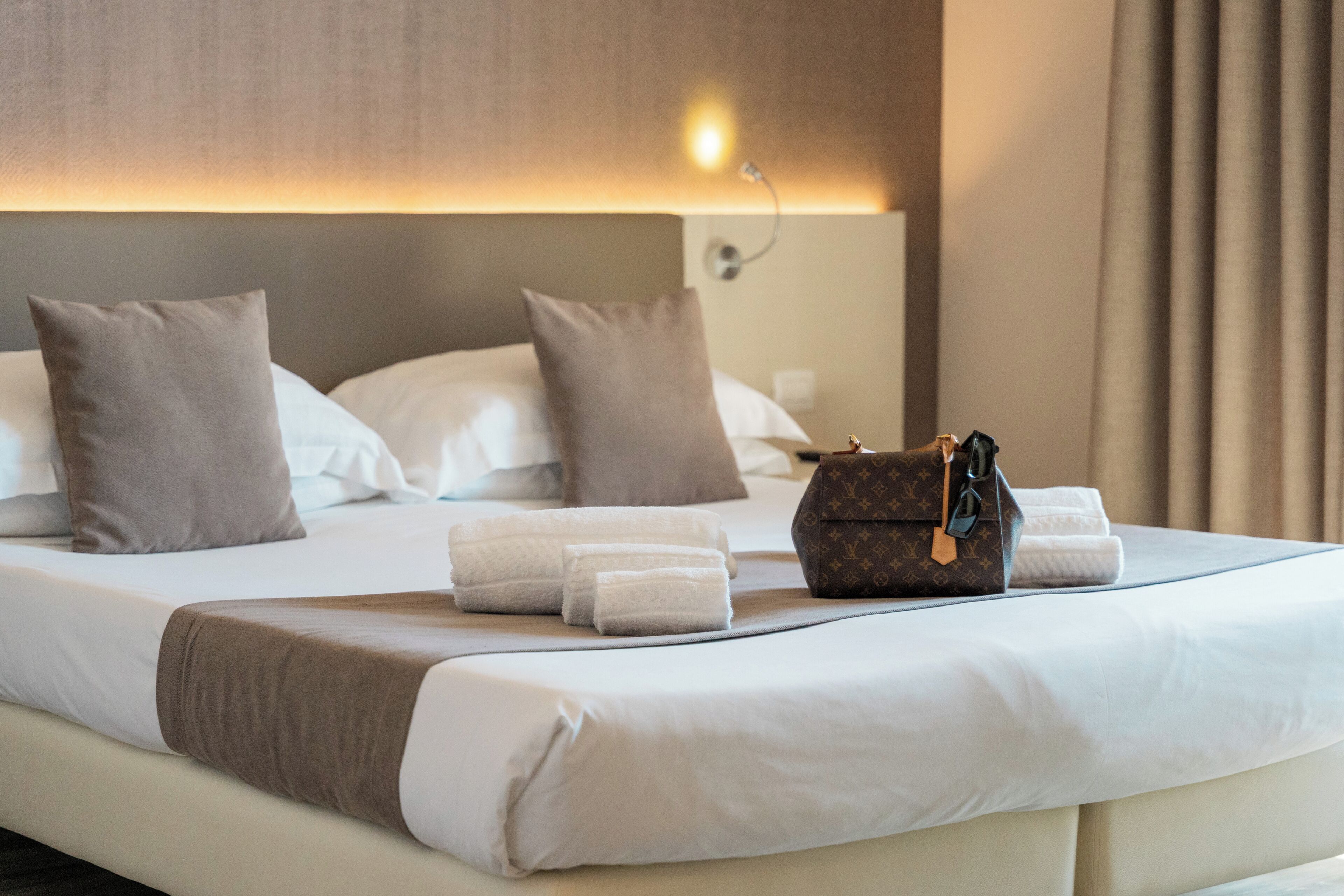 A neatly made bed with pillows, a brown bag, and folded towels.