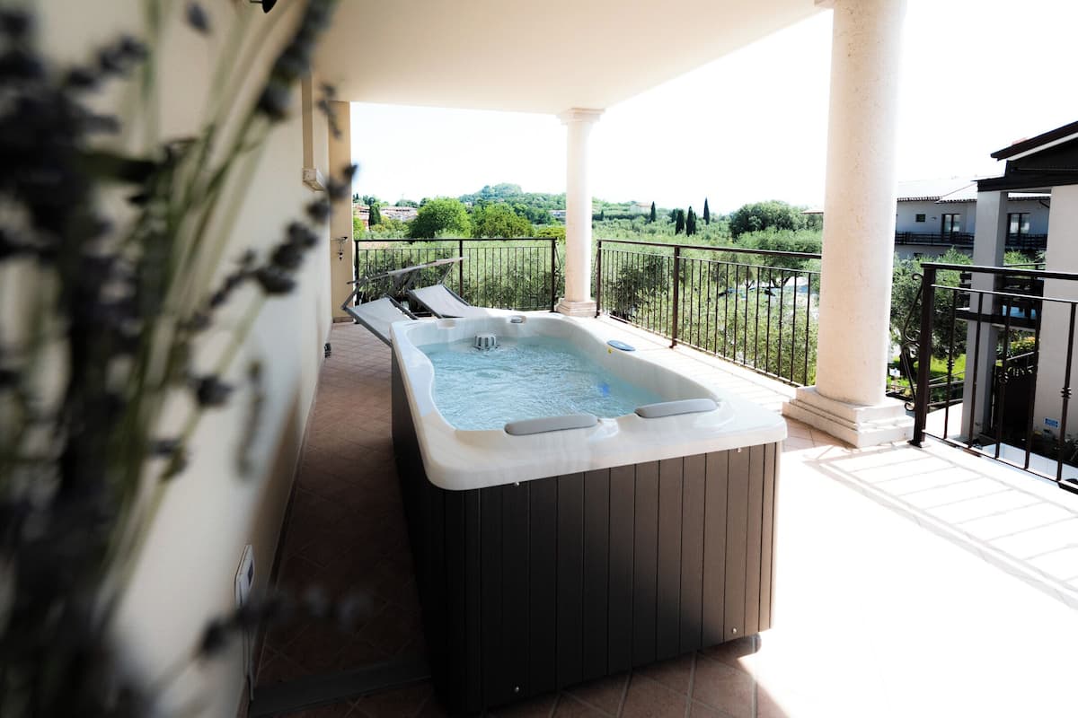 A hot tub on a balcony with a view of greenery and buildings.