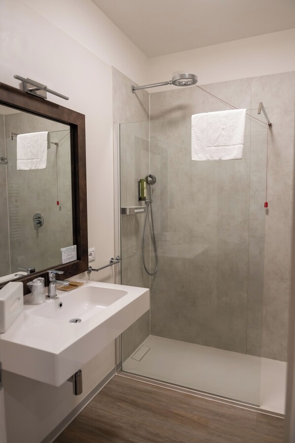 Un baño moderno con ducha acristalada, lavamanos blanco y un espejo grande.