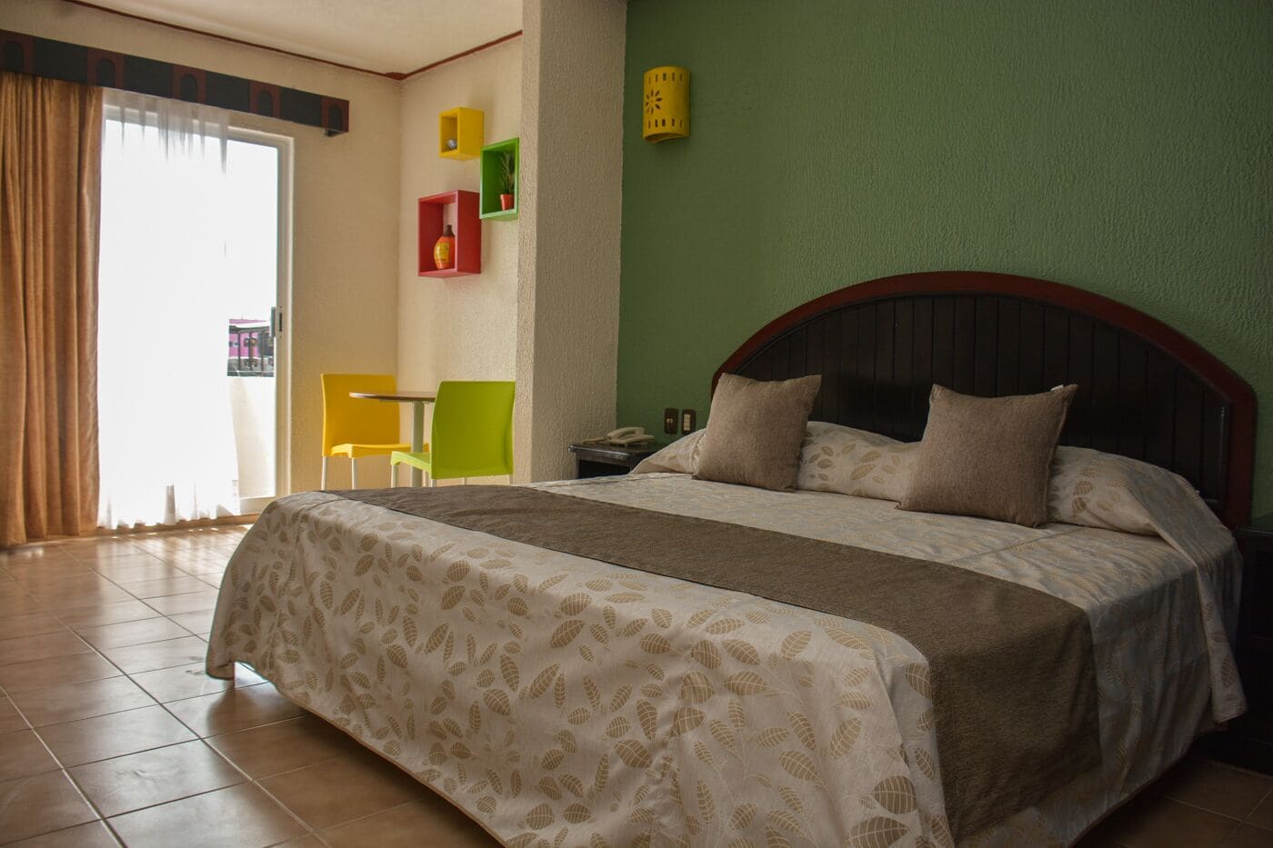 A hotel room with a large bed, a green wall, and a window with curtains.