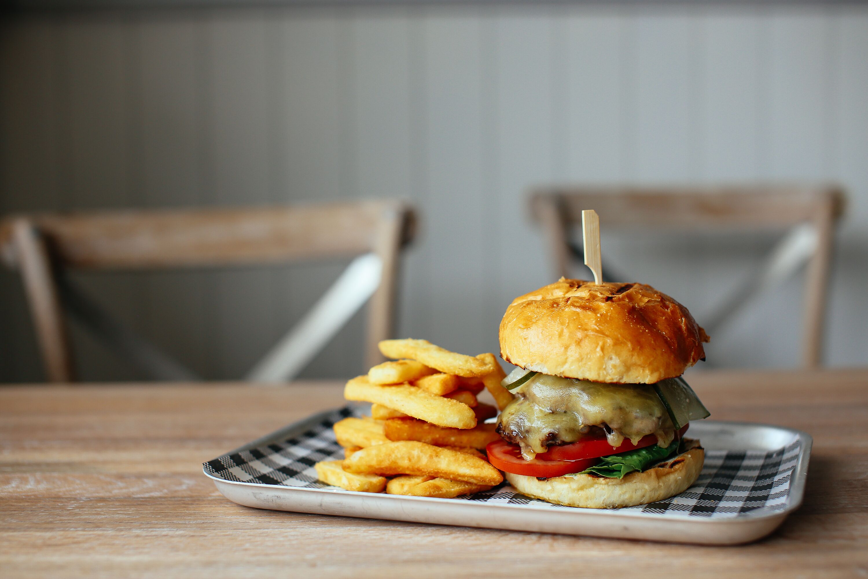 A burger with a toothpick, a side of fries, and a checkered napkin on a wooden table.