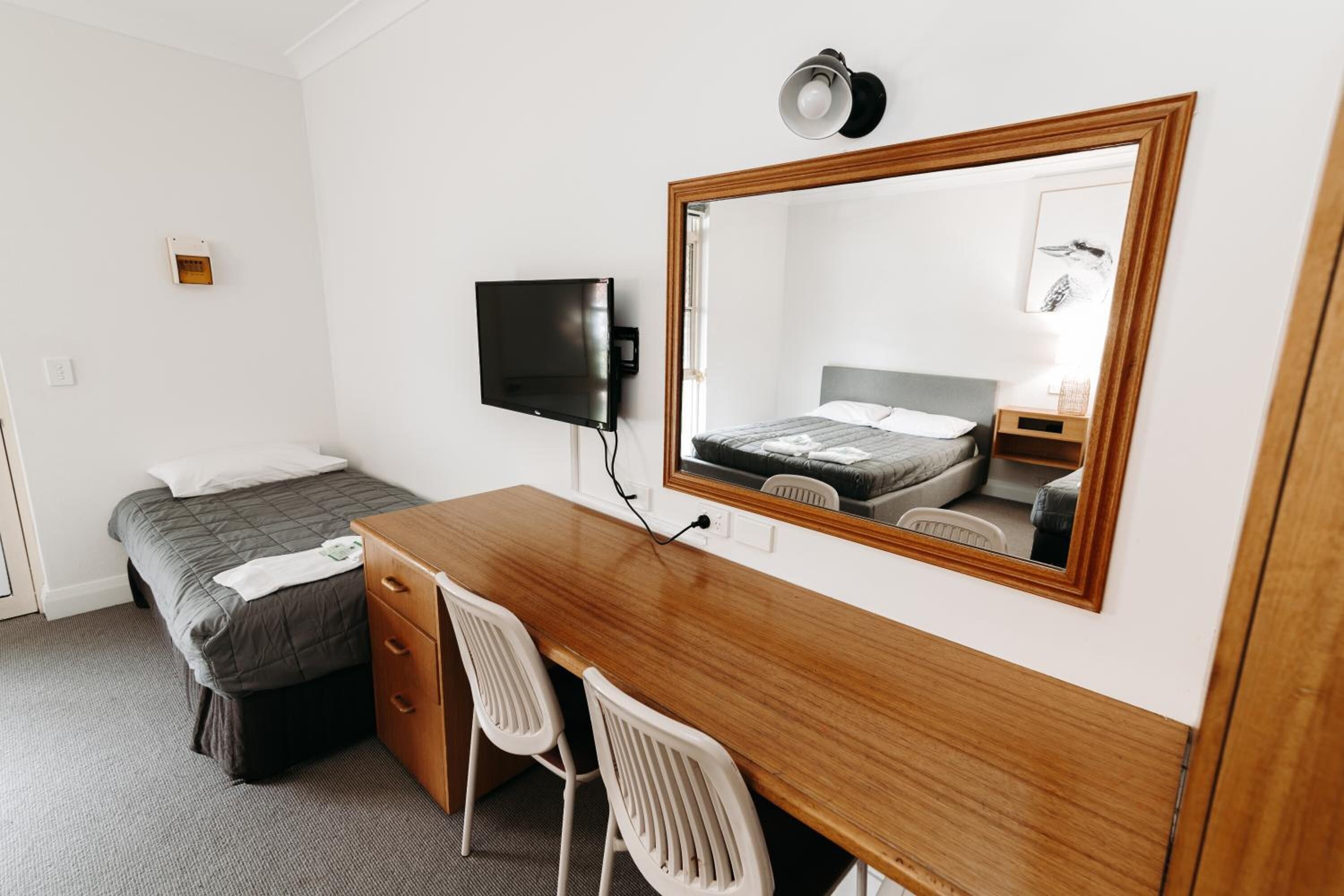 Ein Hotelzimmer mit einem Bett, einem Holztisch mit zwei Stühlen, einem Fernseher und einem großen Spiegel.