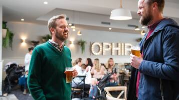 Two men holding glasses of beer in a social setting with other people in the background.