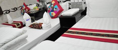 A hotel room with two beds, each with white linens and pillows. There is a small table with toiletries and a decorative pillow.