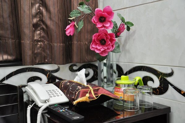 A hotel reception area with a telephone, remote control, a tissue box, a glass jar, and a vase with pink flowers. - Pearl Premium Guest House (Kowloon)