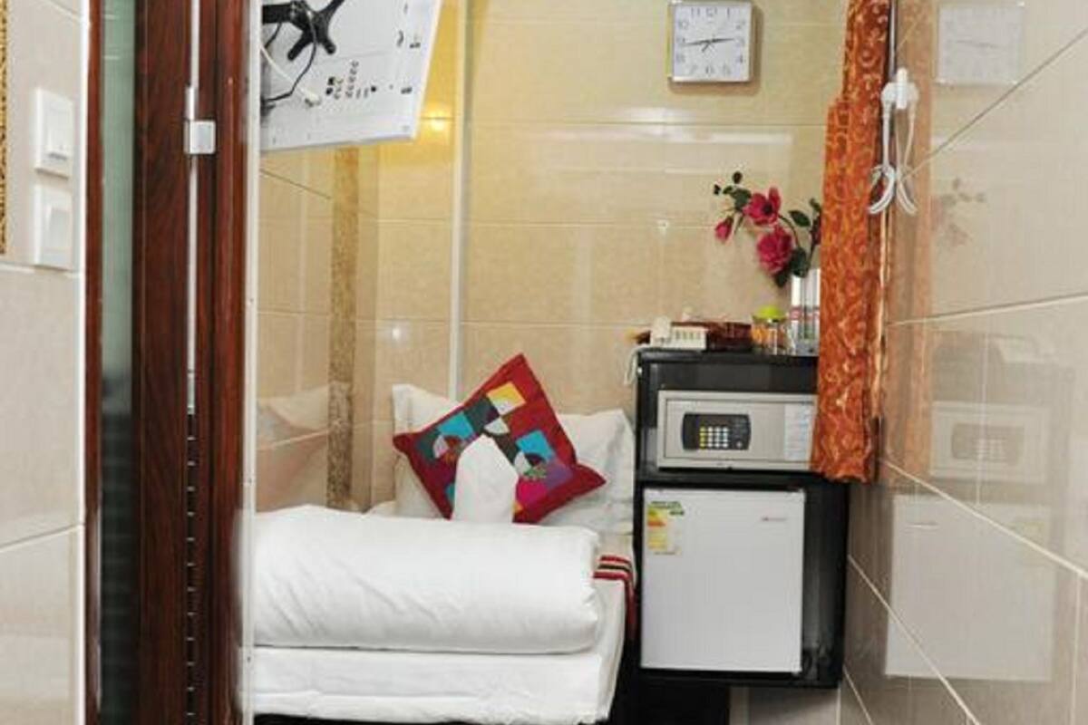 A small, compact hotel room with a bed, a small desk, a microwave, and a clock on the wall.
