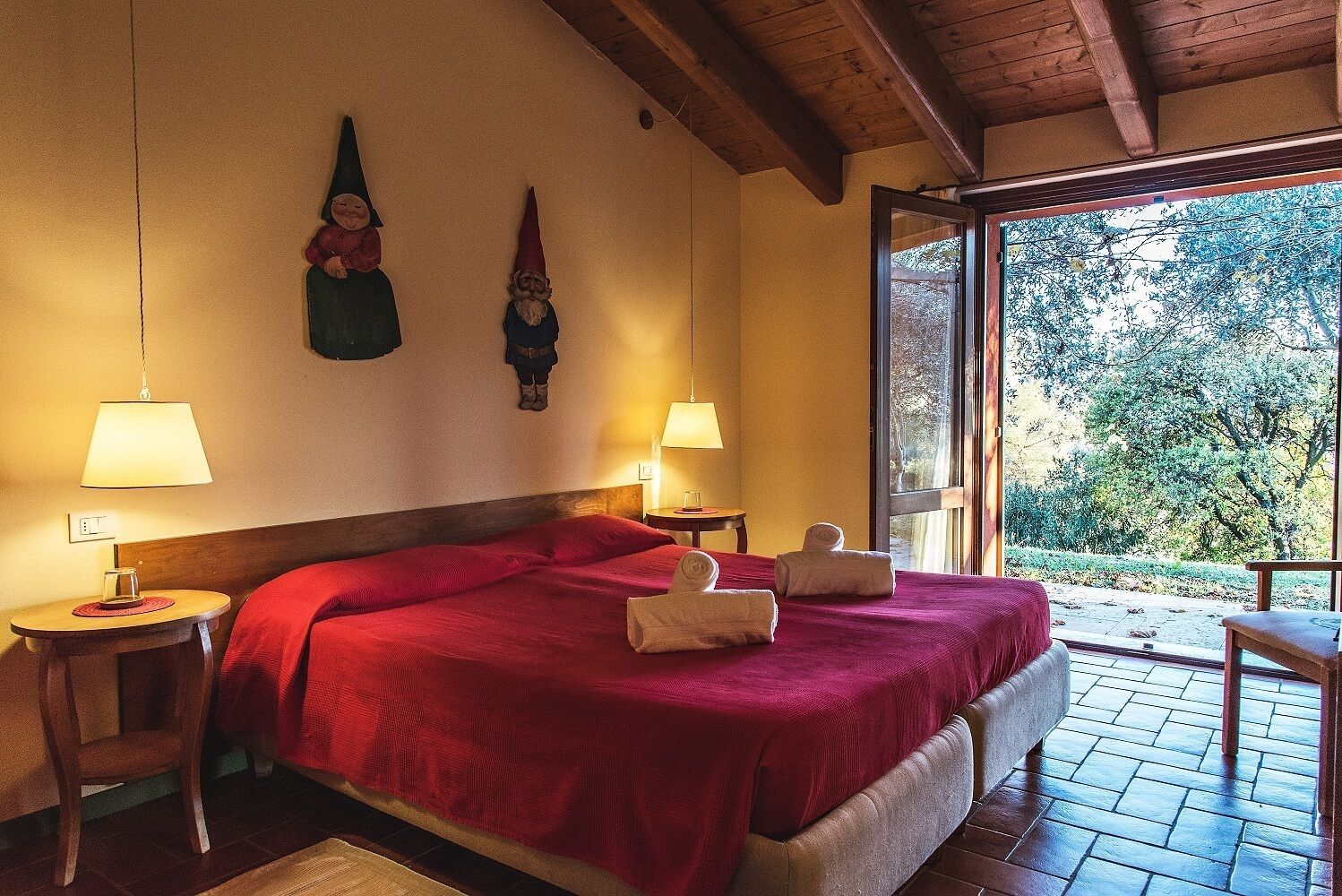 A hotel room with a large bed, two wall-mounted gnome decorations, two bedside lamps, and a view of the outdoors through a glass door.