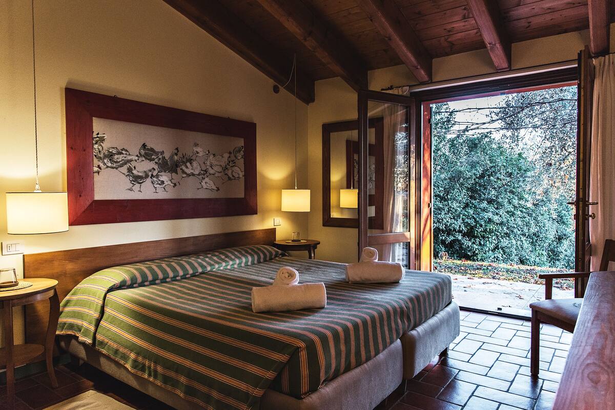 Habitación de hotel con una cama grande, dos mesitas de noche, un cuadro en la pared y vistas al exterior.