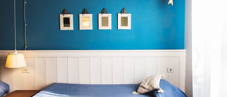 Une pièce avec un mur bleu, un lit recouvert d’une couverture bleue, une table de chevet avec une lampe, et trois tableaux encadrés accrochés au mur.