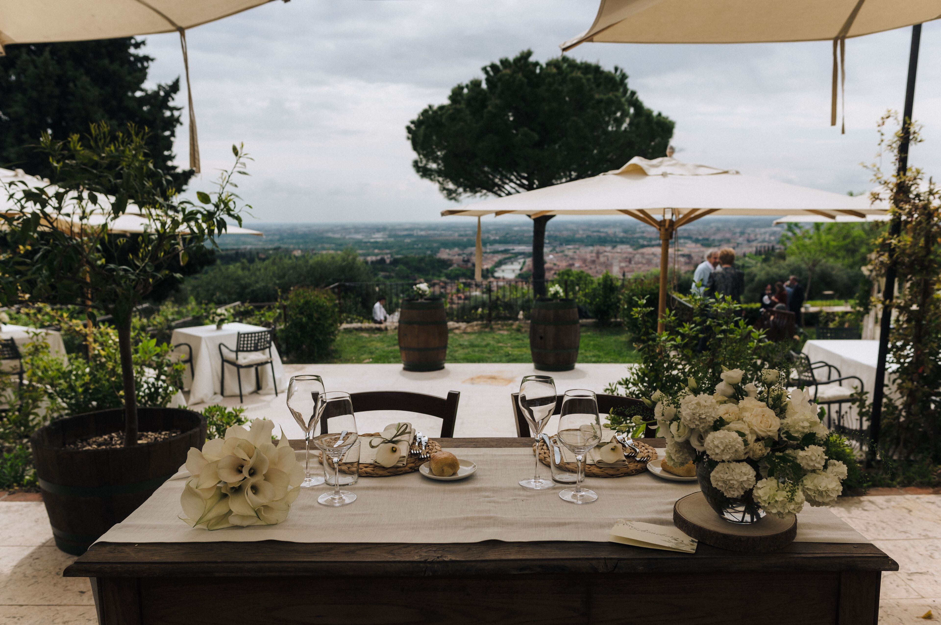 An outdoor dining area with a table set for a meal, surrounded by potted plants and umbrellas.