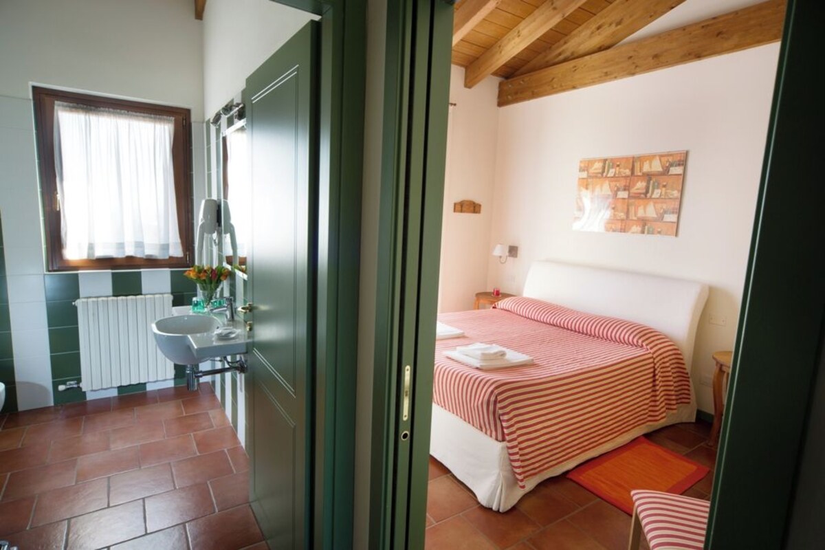 Un dormitorio con cama, mesita de noche, cortinas en la ventana, radiador y una obra de arte en la pared.