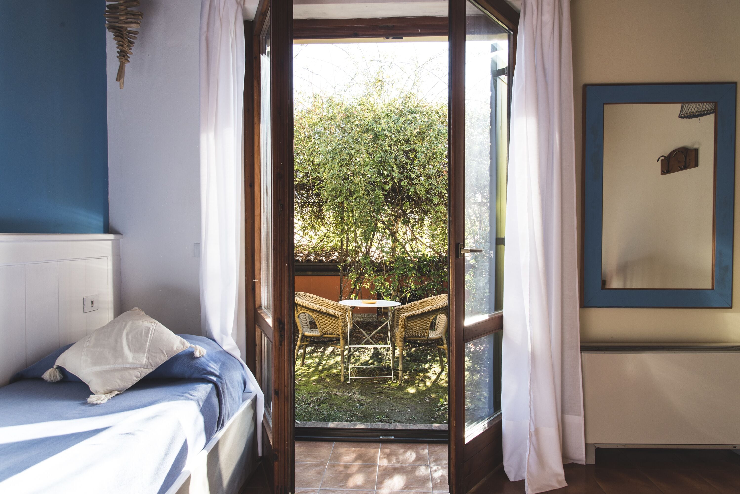 A room with a bed, a small table, and chairs outside a sliding glass door.