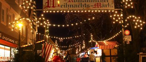 Una escena nocturna en la calle con un letrero que dice 'Romantischer Weihnachtsmarkt' y luces de adorno.