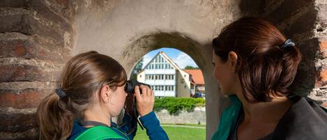 A person taking a photo through a stone archway with a building visible in the background.