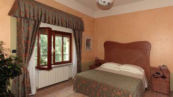 Ein Schlafzimmer mit einem Bett, einem Nachttisch, einer Lampe, einem Heizkörper, einem Fenster mit Vorhängen und einer Deckenleuchte.