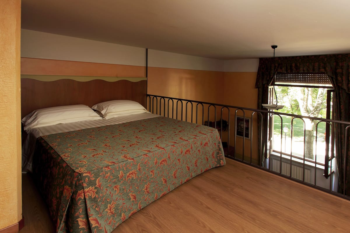 Un dormitorio con cama, ventana con vistas a árboles y barandilla.