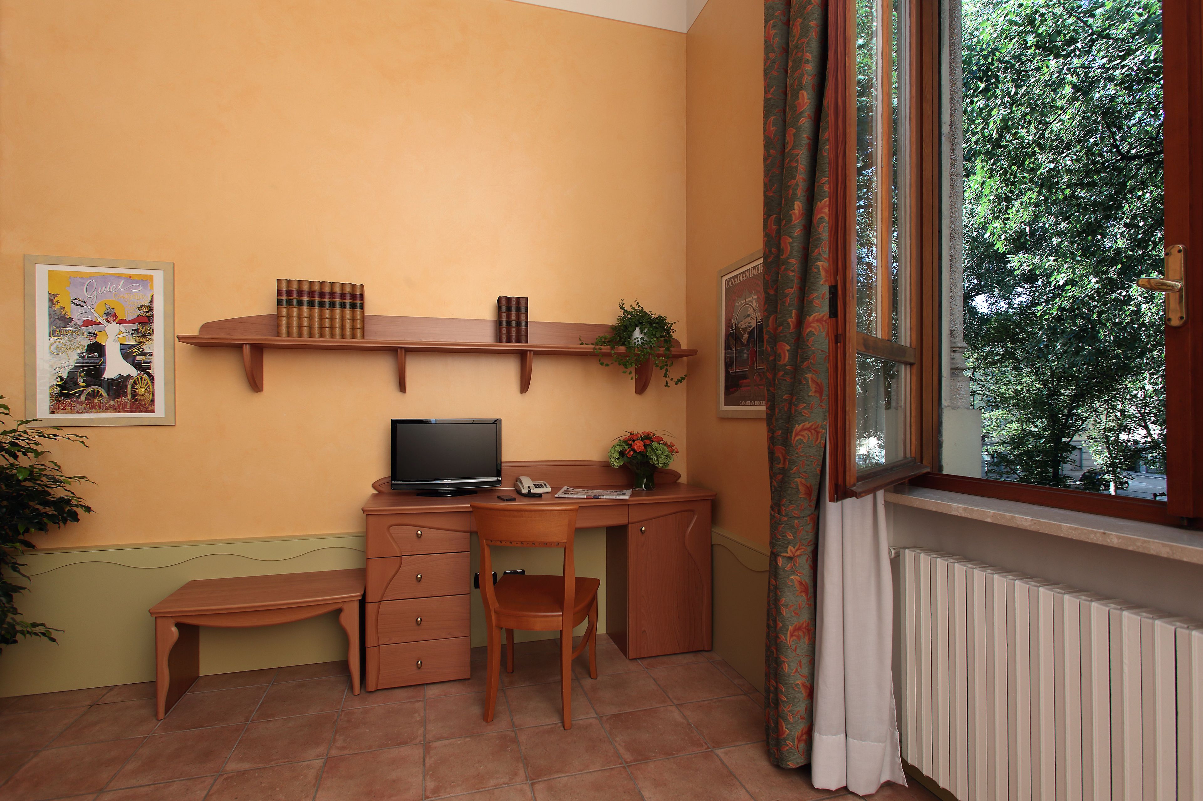 Une petite pièce comprenant un bureau, une chaise, un téléviseur et une fenêtre avec des rideaux.