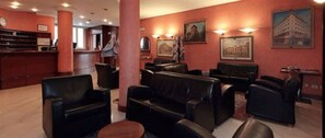 Guests can relax in the hotel lobby's seating area, surrounded by framed pictures and a reception desk.