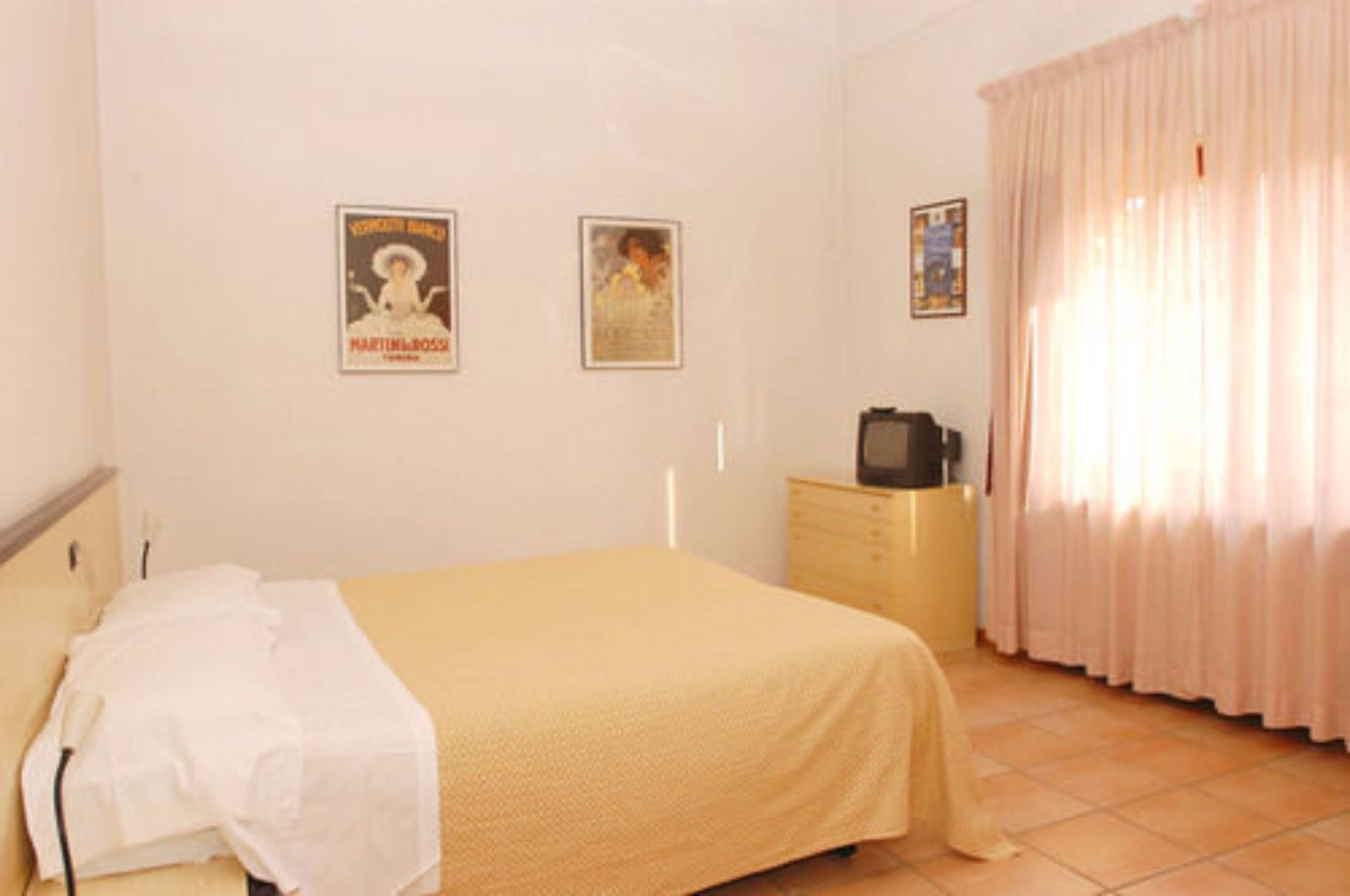 Une chambre à coucher avec un lit, une commode, une télévision et des rideaux.